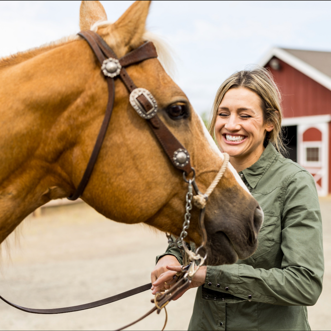 Woman petting a brown horse with a red barn in the background